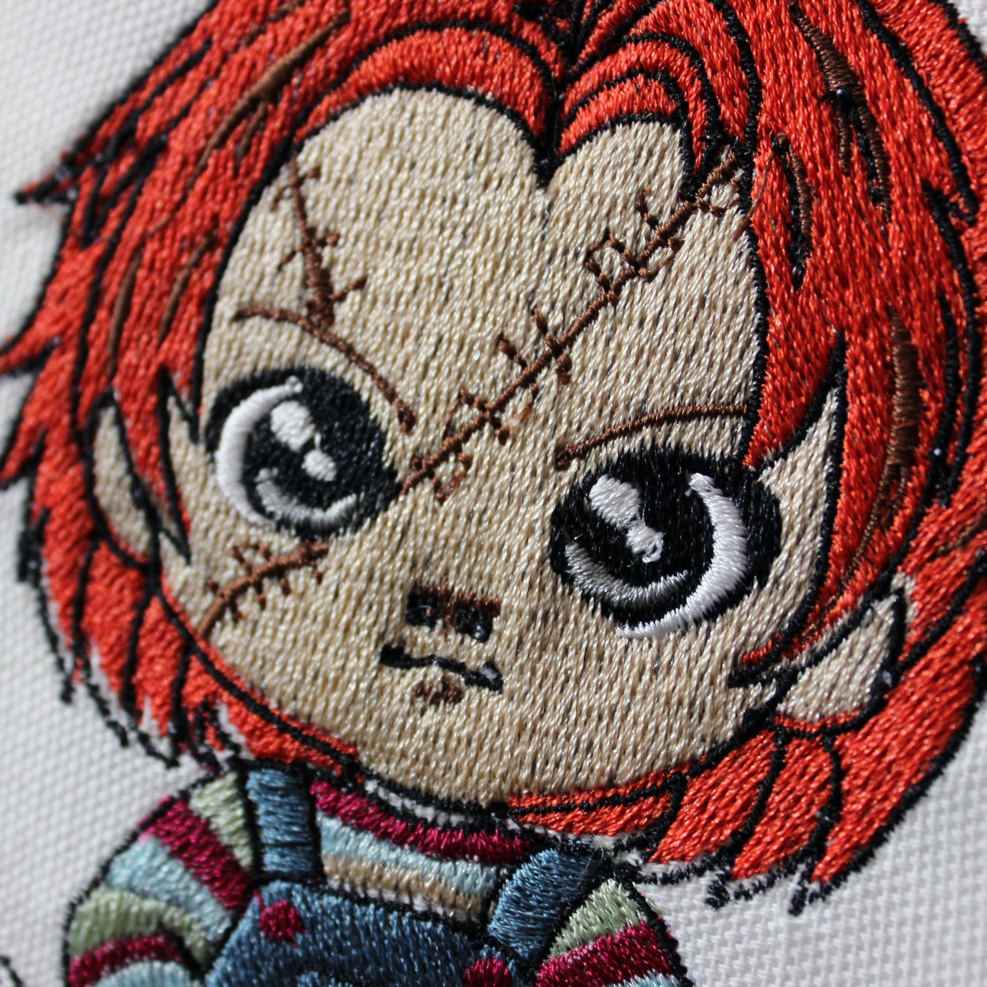 Embroidery of Chucky with red hair and a neutral expression on a white background.