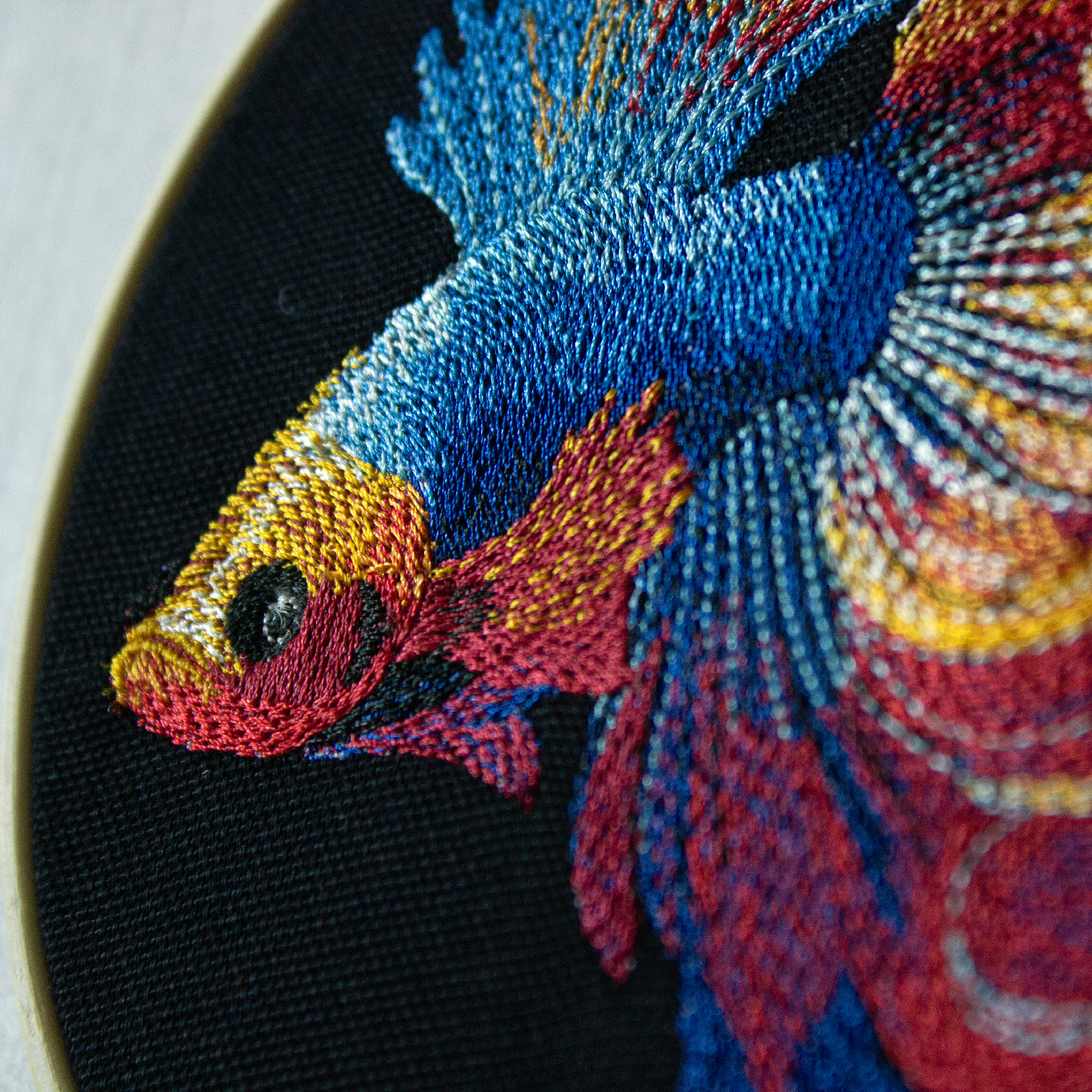 Embroidery of a colorful fish on a black background.