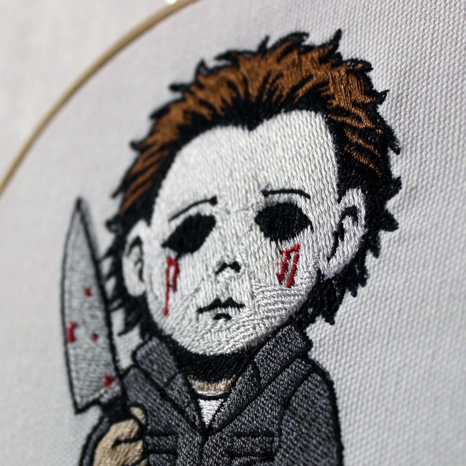 Embroidery of a Michael Myers holding a knife and pumpkin, framed in a hoop.