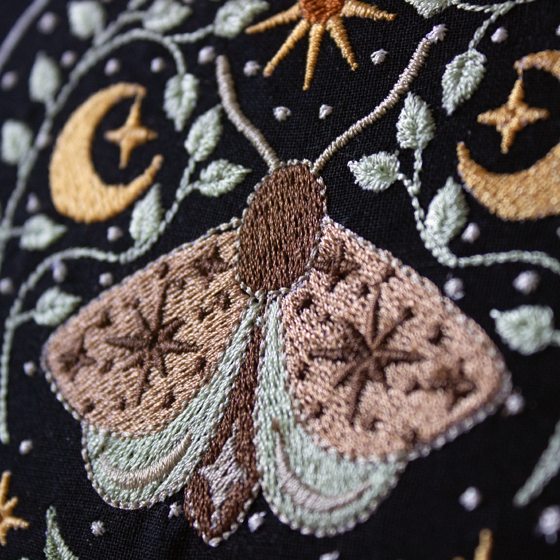 Embroidered moth and celestial design on a dark background