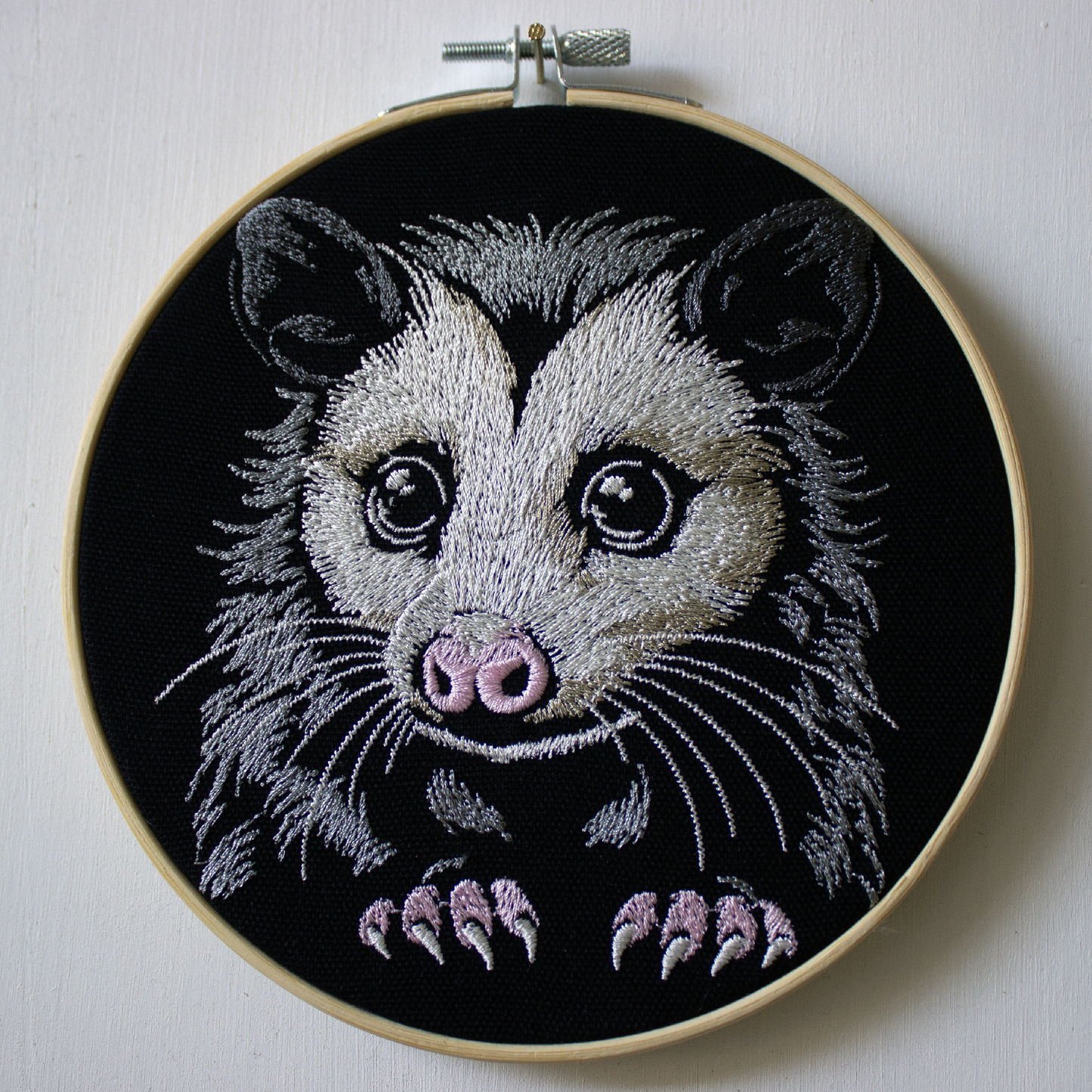A cute embroidered possum with big eyes on a black background.