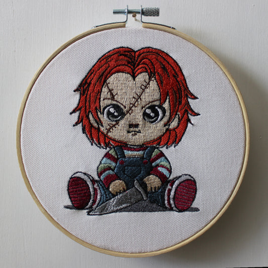 Embroidery of Chucky with red hair and striped shirt in a hoop on a white background.