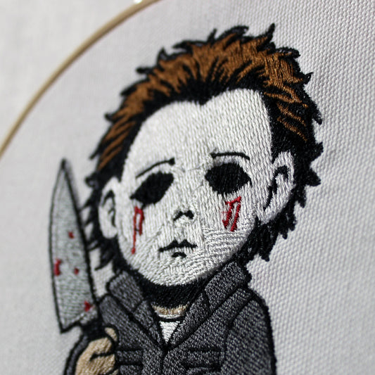 Embroidery of a Michael Myers holding a knife and pumpkin, framed in a hoop.