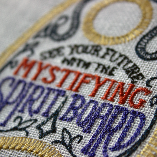 Embroidery hoop with a spirit board planchette on a white background.