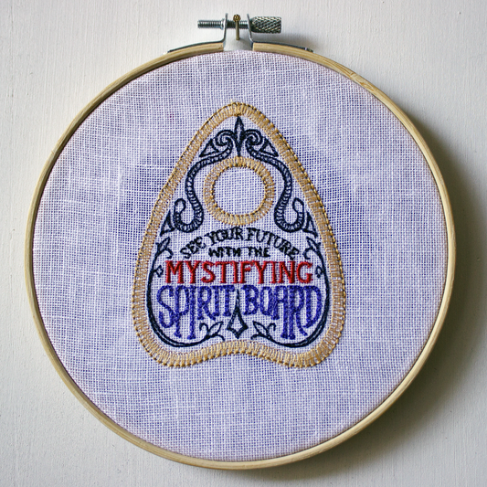 Embroidery hoop with a spirit board planchette on a white background.