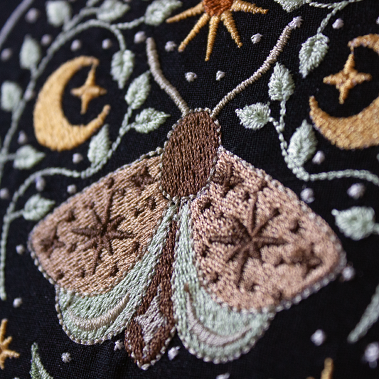 Embroidered moth and celestial design on a dark background