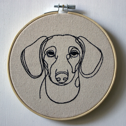 Embroidery hoop with a dachshund portrait on beige fabric.