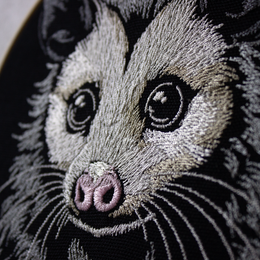 Close-up of an embroidered possum face on fabric.