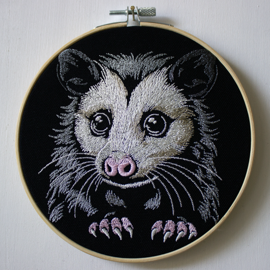 A cute embroidered possum with big eyes on a black background.